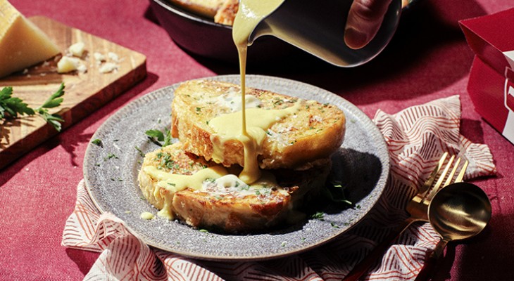 two slices of Parmesan and Parsley French toast with hand pouring hollandaise sauce on top