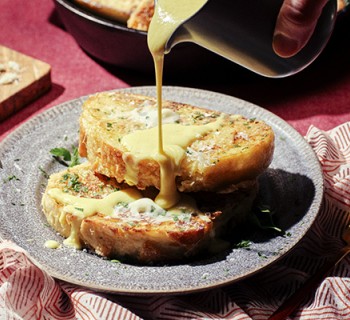 two slices of Parmesan and Parsley French toast with hand pouring hollandaise sauce on top