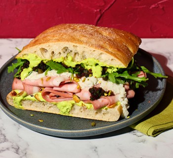 artisan bread Mortadella sandwich on gray plate with green napkin on a marble counter with red stucco wall