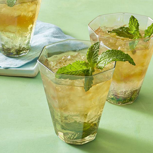 two mint julep cocktails on green background in octagon shaped glasses