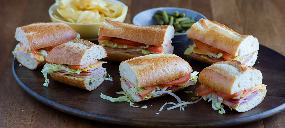 Platter of French Baguette sandwiches with a bowl of chips and pickles