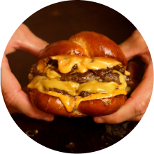 Close-up of hands holding a double cheeseburger with melted cheese and a pretzel bun