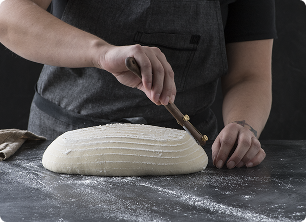 A baker scoring a loaf of sourdough by hand