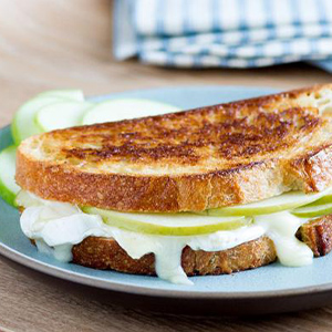Close-up of baked brie grilled cheese made with green apple, honey dijon, and French Loaf slices on a plate
