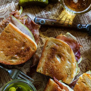 Overhead image of Apple Chutney, prosciutto, and pear with gruyere and Tuscan Loaf bread on a tray with various serving utensils