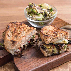 Portabella mushroom and veggie grilled cheese on a wood tray with a side of mushrooms and veggies