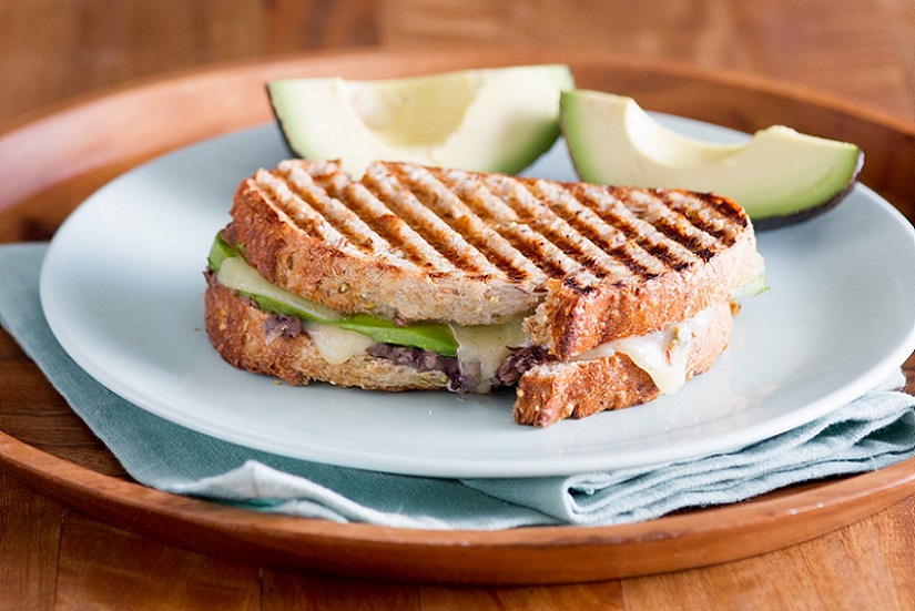 Mexi vegetarian panini sitting on white plate with two slices of avocado