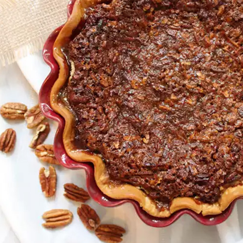 Cooked derby pie on white table cloth with pecans scattered around the dish