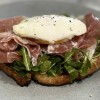 Tartine with prosciutto, arugula and poached egg on 8 grain artisan bread