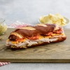 A sandwich made on a pretzel roll with layers of sliced turkey, cheddar cheese, and roasted tomatoes. The sandwich is served on a wooden cutting board with potato chips and mustard sauce visible in the background.