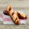 Fresh pretzel baguettes with a distinctive golden-brown shiny crust and classic slash marks on top, arranged on a red and white striped cloth napkin on a wooden surface.