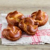 Soft and glossy pretzel rolls with a deep brown color, resting on a folded kitchen towel over a wooden table.