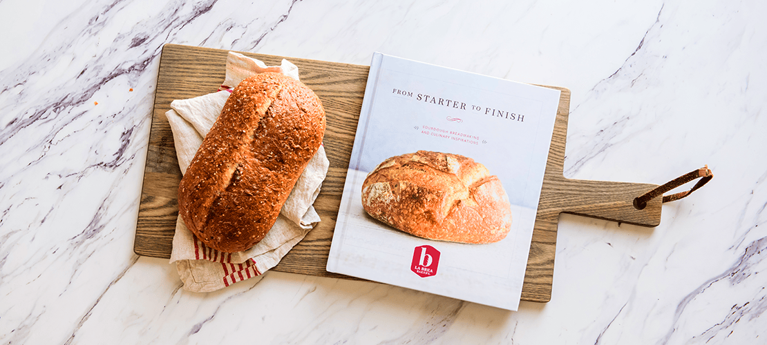 Overhead view of La Brea cookbook on a wood cutting board beside a loaf of artisan bread