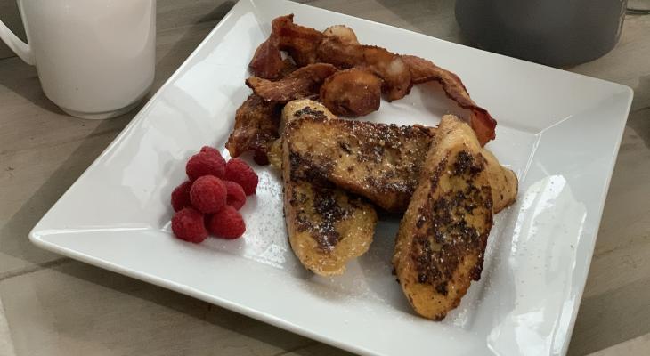 Cup of coffee next to plate filled with Eggnog French Toast, berries and bacon