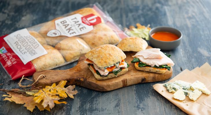 Buffalo Turkey Sliders on La Brea Bakery Seed Sourdough Rolls on a Cutting Board with Sides and a Bag of Rolls