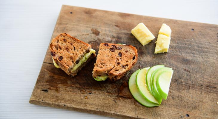 Grilled Cheese made with Cinnamon Raisin Loaf on a cutting board with green apple slices and honey