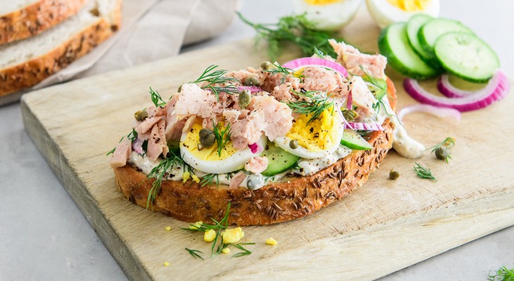 open faced tuna sandwich on wood serving board with sliced artisan bread in background