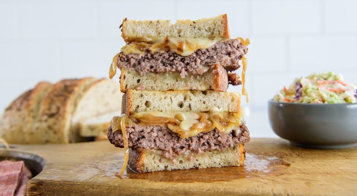 Patty melt sandwich cut and stacked on wood cutting board