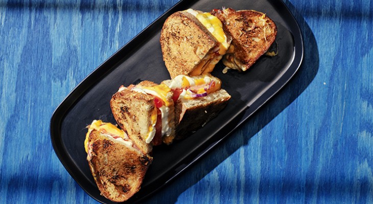 Sliced Grilled tomato, onion and cheese toasty on rosemary loaf sandwiches on black serving plate with blue background