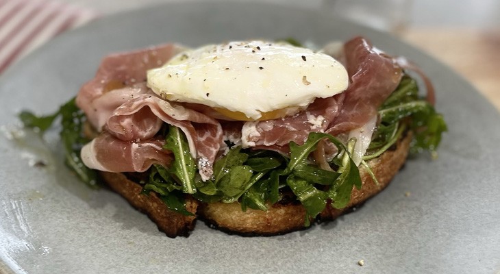 Tartine with prosciutto, arugula and poached egg on 8 grain artisan bread