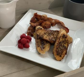 Cup of coffee next to plate filled with Eggnog French Toast, berries and bacon