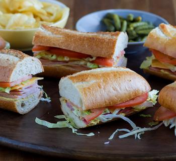 Platter of French Baguette sandwiches with a bowl of chips and pickles