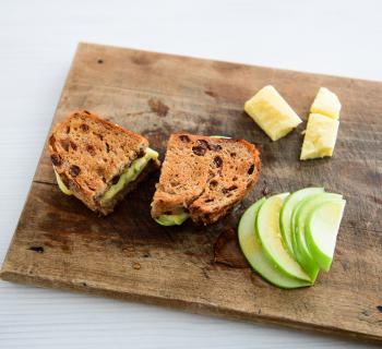 Grilled Cheese made with Cinnamon Raisin Loaf on a cutting board with green apple slices and honey