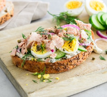 open faced tuna sandwich on wood serving board with sliced artisan bread in background