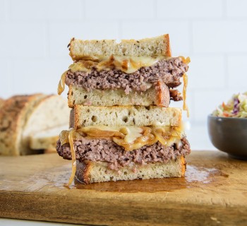 Patty melt sandwich cut and stacked on wood cutting board