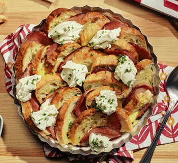 Dish of eggs Benedict casserole cooked inside a metal tin on a butcher block counter