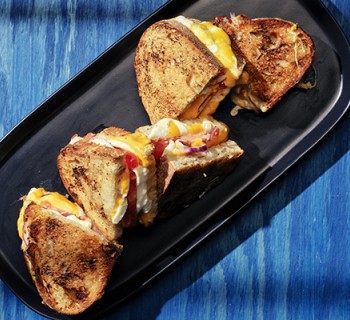 Sliced Grilled tomato, onion and cheese toasty on rosemary loaf sandwiches on black serving plate with blue background