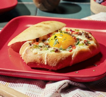 Breakfast bowl made of French dinner roll with sausage and eggs on red square plate