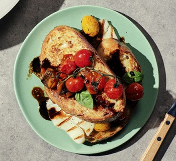 Two slices of rosemary round savory french toast topped with oasted tomatoes and halloumi on a green plate and concrete background