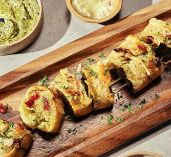 Sliced Sun dried tomato and pesto garlic bread on wood serving board with spices and sauce