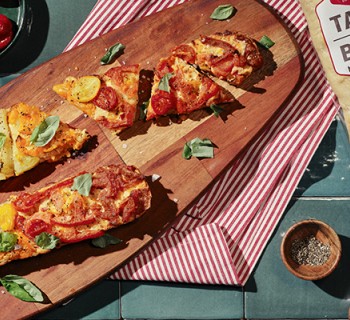 Tomato pie baguette pizza on a wood serving board with a pack of La Brea Take and bake baguette artisan bread