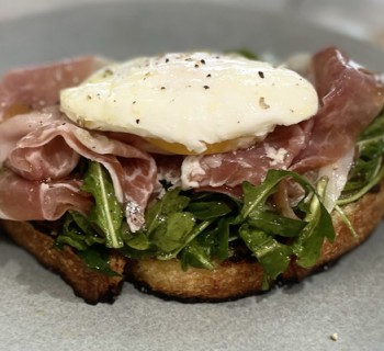 Tartine with prosciutto, arugula and poached egg on 8 grain artisan bread