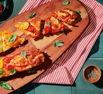 Tomato pie baguette pizza on a wood serving board with a pack of La Brea Take and bake baguette artisan bread